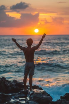 A man standing on a rock with his arms outstretched at the ocean