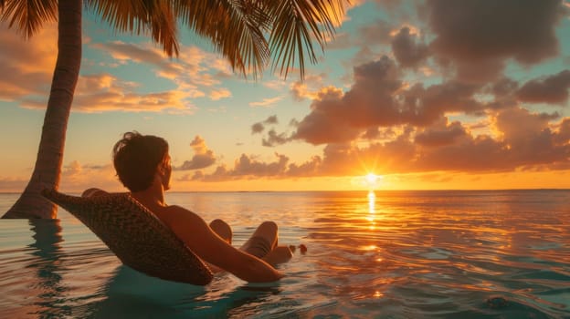 A man sitting in a chair under the palm tree at sunset