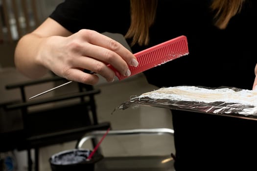 Beauty sphere. Highlighting. Air touch. Hair coloring in a beauty salon. A master hairdresser-colorist dyes a client's brown hair blond. Apply lightening powder to hair on foil with a brush. Close-up.