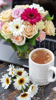 A cup of coffee and flowers on a laptop next to each other