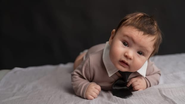 Portrait of a baby lying on his stomach wearing a tie on a black background
