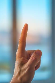 A man holding up his finger in front of a window