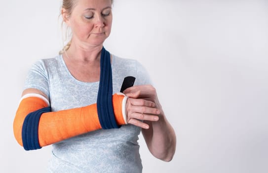 middle aged woman with broken arm in cast hangs her arm in a sling, modern treatment methods, on a neutral background, copy space, high quality photo