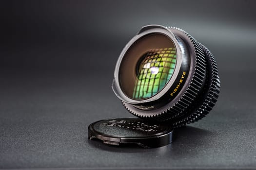 Tilted view of a fisheye lens showing colorful light refractions, yellow fisheye text, essential for wide-angle photography, against dark background