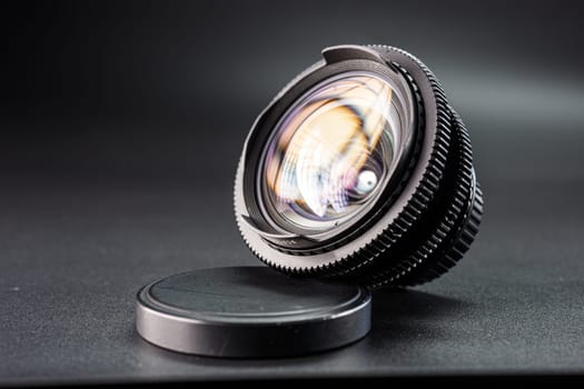 Artistic view of a vintage lens with vibrant reflections, focus on detailed ring textures, essential photography equipment on dark surface with lens cap