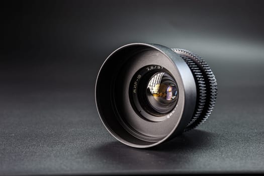Precision-engineered camera lens angled to show reflections, details of aperture marking 2.8 37 visible, set on dark surface for photographic showcase.