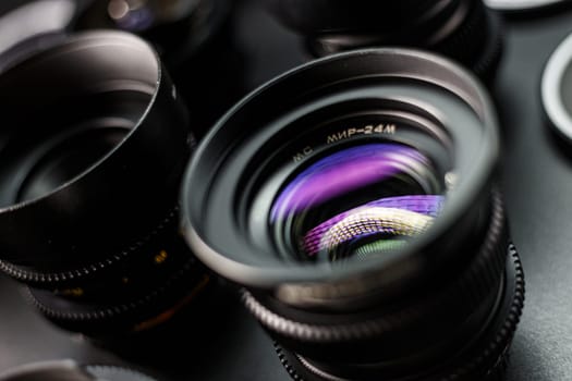 Close-up of a vintage MC lens showing colorful light patterns, surrounded by a collection of camera lenses with blurred edges, photography equipment showcase.