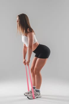 Caucasian woman doing exercises with fitness elastic band on white background. Vertical photo