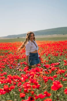 Happy woman in a poppy field in a white shirt and denim skirt with a wreath of poppies on her head posing and enjoying the poppy field