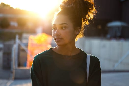Back lit young pensive African American woman outdoors during sunset. Lifestyle concept.