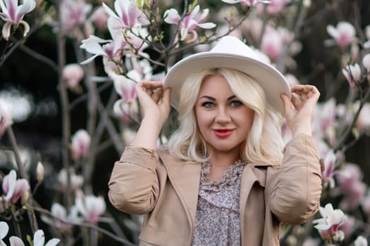 Magnolia flowers woman. A blonde woman wearing a white hat stands in front of a tree with pink flowers. She has a smile on her face and she is enjoying the beautiful scenery