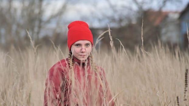 Portrait of a teenage girl in glasses standing in tall grass in the fall