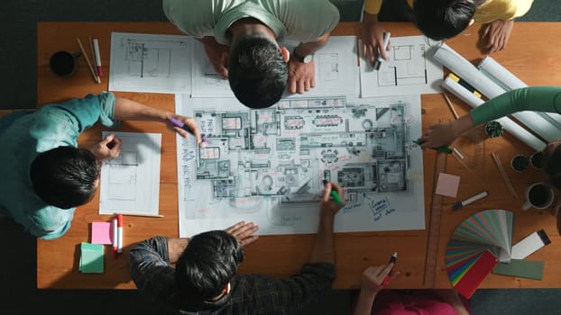 Top down view of civil engineer team writing at blueprint at meeting table with color palettes. Group of diverse people planning and taking a note while manager looking at project plans. Symposium.