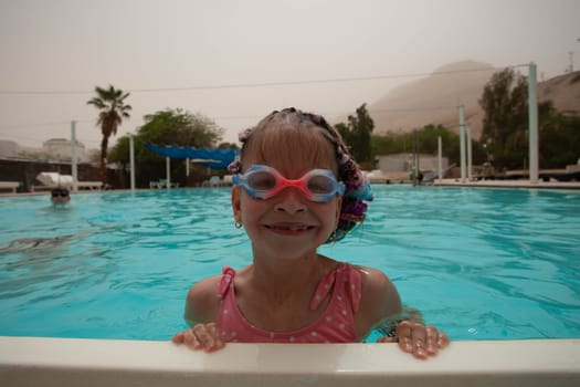 A girl with glasses and bright pigtails swims in the pool. High quality photo