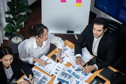 Wide top view of diverse group of business analyst team analyzing financial data report paper on meeting table. Chart and graph dashboard by business intelligence analysis. Meticulous