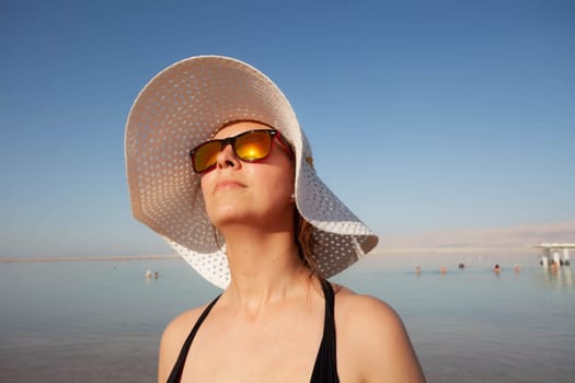 A girl in sunglasses basks in the sun against the background of the Dead Sea. High quality photo