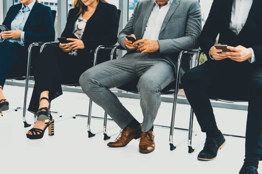 Businesswomen and businessmen using mobile phone while waiting on chairs in office for job interview. Corporate business and human resources concept. uds