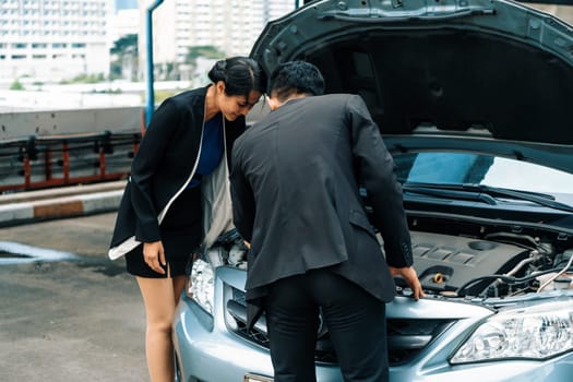 Man help woman fix the car problem. He pop up the car hood to repair the damaged part. uds