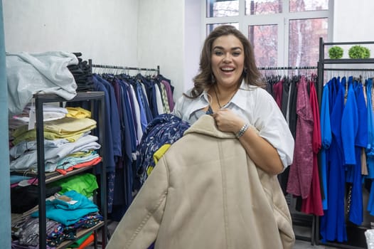 Happy fat woman holding armful of clothes in plus size store