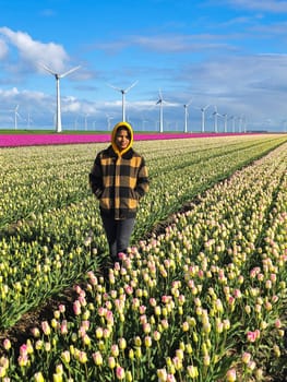 A woman gracefully stands in a vibrant field of tulips, surrounded by bursts of colorful petals under the Dutch windmill turbines in Spring in the Noordoostpolder Netherlands
