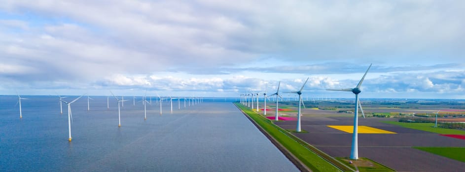 A serene scene unfolds as wind mills stand tall around a vast lake, harnessing the power of the wind in the Netherlands during Spring. windmill turbines in the ocean with colorful flower field on land