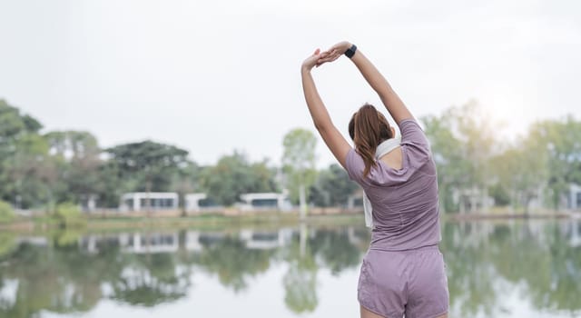 Asian woman is stretching her arms out in front of a lake.