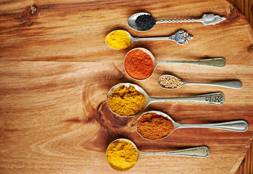 Spoons, spice and selection of ingredients for seasoning on kitchen table, turmeric and paprika for meal. Top view, condiments and options for cooking in Indian culture, cumin and food preparation.