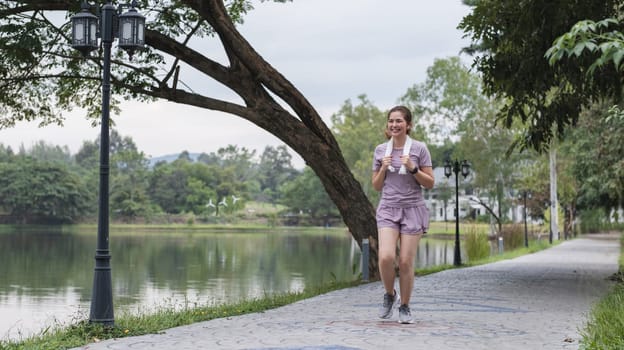 A woman is running on a path near a lake. She is smiling and holding a cup. The scene is peaceful and serene, with the water reflecting the trees and the sky