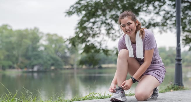 A woman is sitting on the ground and tying her shoe. She is smiling and she is enjoying herself