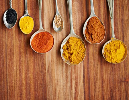 Spoons, spice and selection of flavor for seasoning on kitchen table, turmeric and paprika for meal. Top view, condiments and options for spicy cooking in Indian culture, cumin and food preparation.