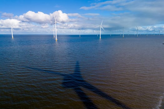 A vast body of water glistens under the spring sunlight as wind turbines stand tall in the background, harnessing the power of the wind. windmill turbines in the ocean of the Netherlands