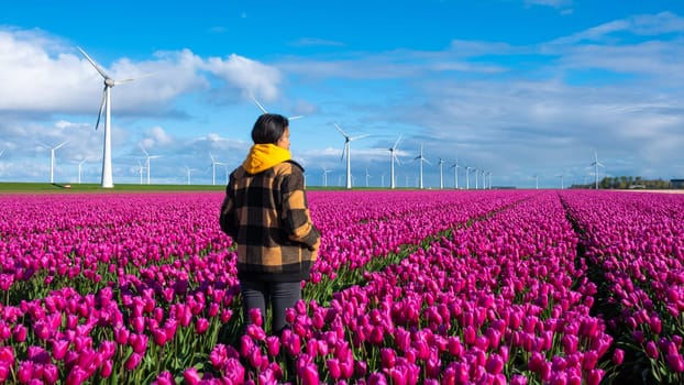 An Asian woman stands gracefully amidst a vast field of vibrant purple flowers under the gentle Spring sunlight. women in a field of tulip flowers in the Noordoostpolder Netherlands