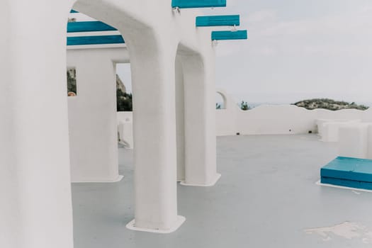 A white building with blue accents, and the blue accents are on the pillars. The building is located near the ocean, and the blue accents give it a unique and interesting appearance