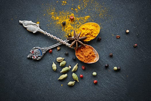 Above, spices and spoon for flavor and dry ingredient for cooking, cuisine and food on table top for traditional Indian dish. Turmeric and curry powder with peppercorns and cardamom for hot dinner.