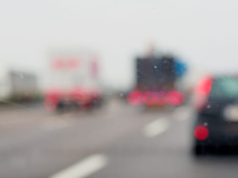 A blurry image of a busy street with cars and a truck. The rain is making the windshield of the cars and truck wet