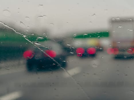 A blurry image of a busy street with cars and a truck. The rain is making the windshield of the cars and truck wet