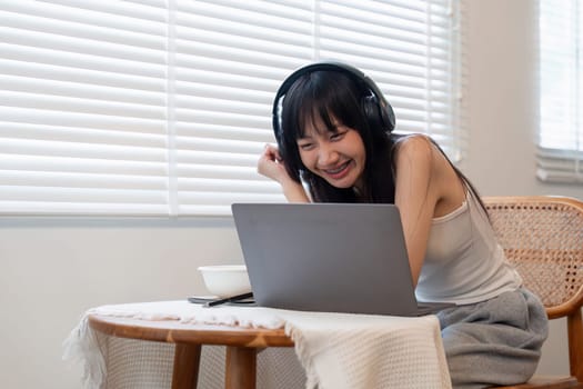 Young woman using laptop computer and wearing headphone at home.