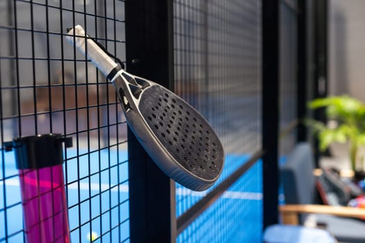 Black professional paddle tennis racket and ball with natural lighting on blue background. Horizontal sport theme poster, greeting cards, headers, website and app. High quality photo