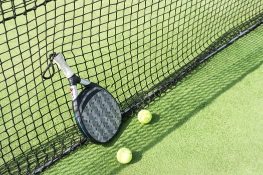 Padel racket and padel ball on a green court in the sunset. High quality photo