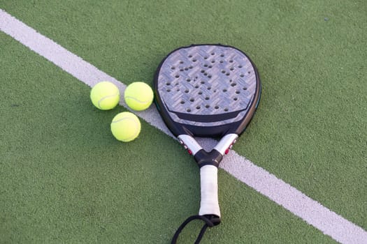 Yellow balls on grass turf near padel tennis racket behind net in green court outdoors with natural lighting. Paddle is a racquet game. Professional sport concept with copy space. High quality photo
