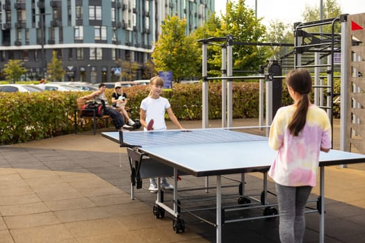 Young teenager girl playing ping pong. She holds a ball and a racket in her hands. Playing table tennis outdoors in the yard. High quality photo