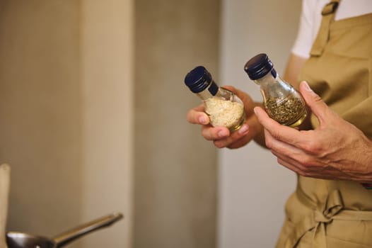 Close-up chef hands holding two glass bottles with condiments for seasoning dish while cooking dinner