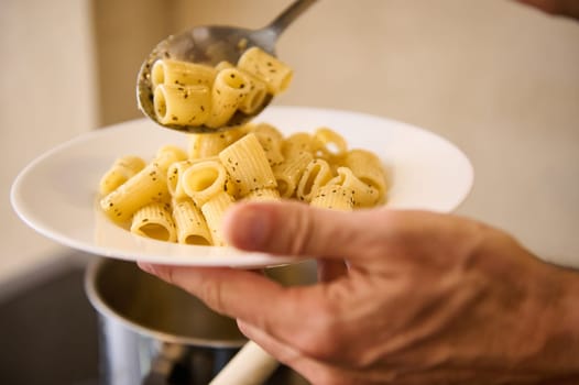 Close-up pouring Italian pasta on white plate before plating up and serving to the customers. Chef holds plate with freshly cooked Italian pasta