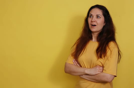 Beautiful woman in yellow T-shirt with long dark hair opened her mouth in surprise. Portrait of a surprised beautiful woman with the expectation of darkness in a yellow tank top on a yellow background.