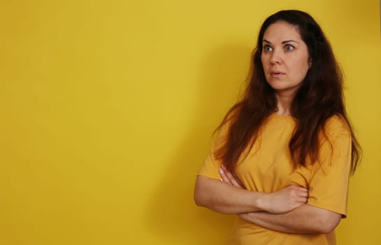 A beautiful woman in a yellow T-shirt with long hair in a state of bewildered surprise. Woman posing with her arms crossed.