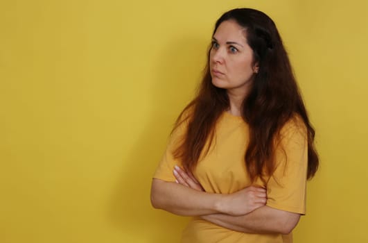 Beautiful woman in yellow t-shirt on yellow studio background with long dark hair. Portrait of a surprised beautiful woman.