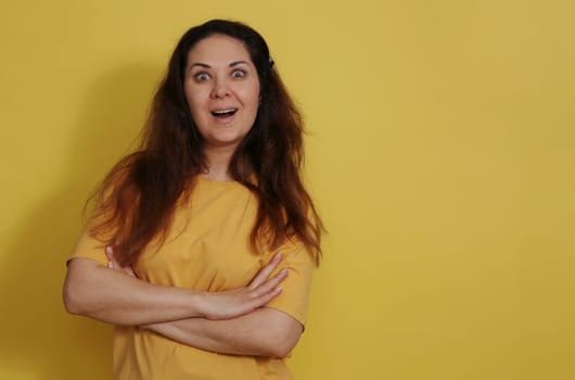 Close-up portrait of a charming surprised woman in a cotton t-shirt, good reaction to the news. The reaction of a woman in a yellow T-shirt on a yellow background received a pleasant unexpected news.