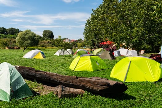 A vibrant campsite with colorful tents scattered across a lush green field, under a clear blue sky