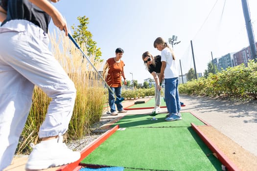 Cute school girl playing mini golf with family. Happy toddler child having fun with outdoor activity. Summer sport for children and adults, outdoors. Family vacations or resort. High quality photo