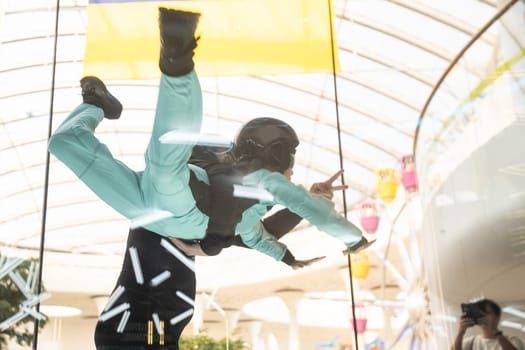 Excited teenage girl in helmet flying in aerodynamic tube wind tunnel. Skydiving training. High quality photo